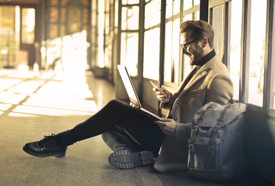 Smiling businessman sitting on the floor with a laptop and a smartphone, working